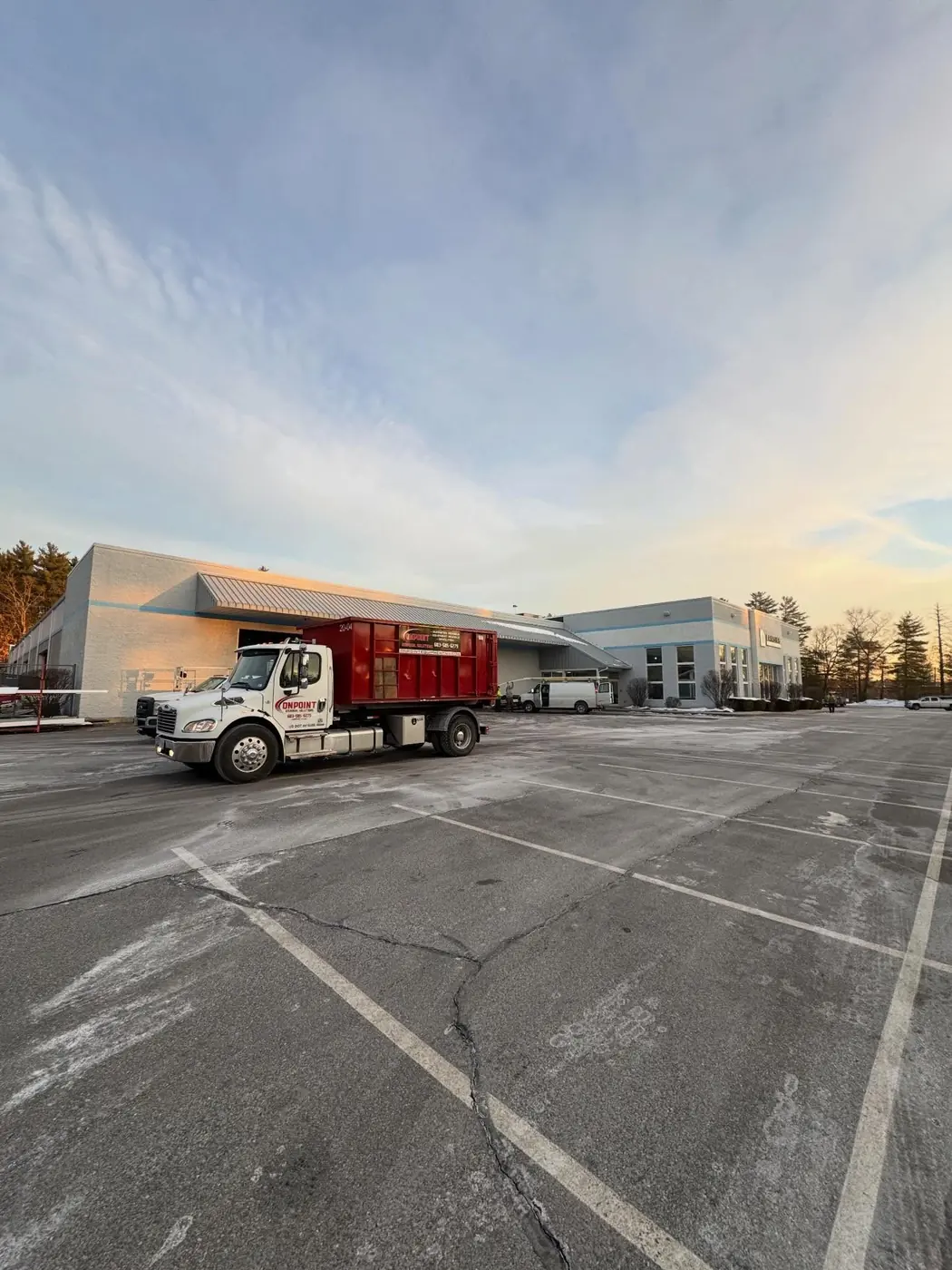 Onpoint roll off truck delivering a dumpster to a commercial building at sunrise