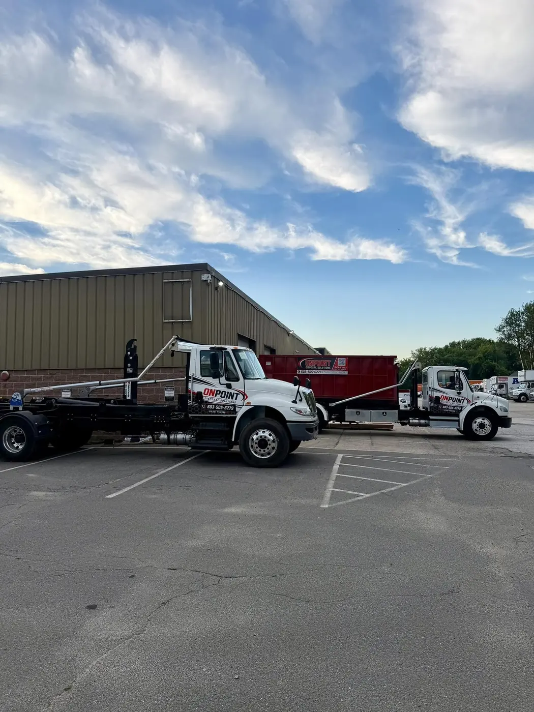Two Onpoint Disposal Solutions roll off trucks and a red dumpster at the company yard